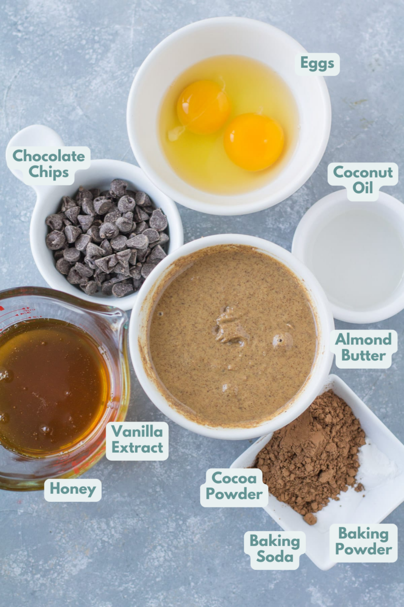 An overhead shot of ingredients for almond butter brownies in small white bowls on a grey background.