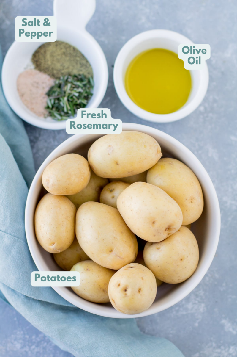 Ingredients for crispy smashed potatoes in small white bowls on a grey background: baby potatoes, olive oil, salt, freshly ground black pepper, fresh rosemary
