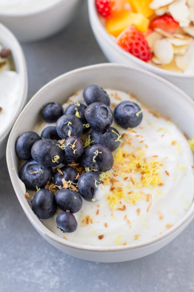 A close up of a blueberry yogurt bowl in a white small bowl on a grey background