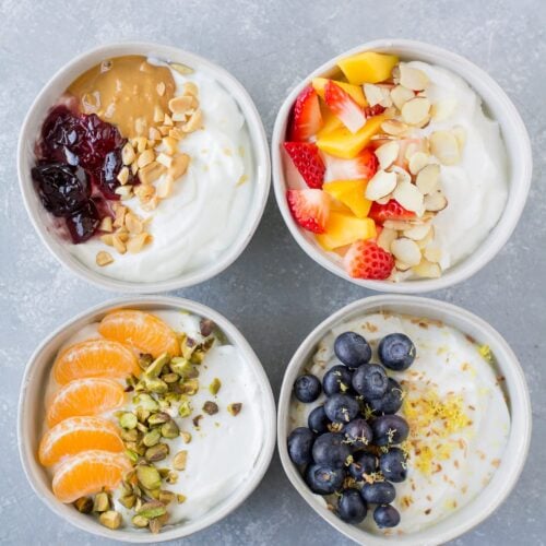 An overhead shot of 4 healthy yogurt bowls on a grey background