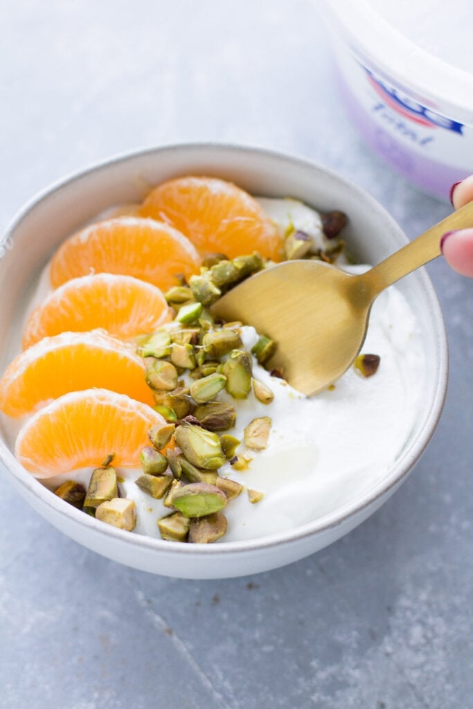 A close up of Orange Pistachio healthy yogurt bowl on a grey background