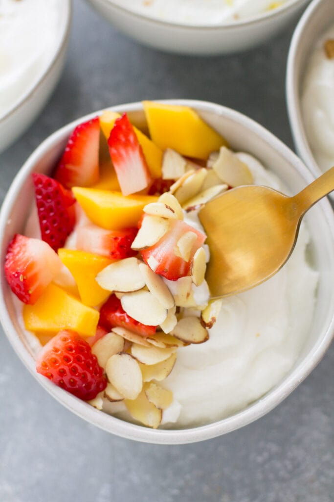 A gold spoon taking a bite out of a healthy strawberry yogurt bowl