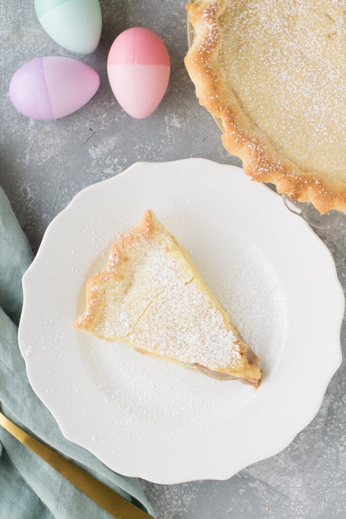 An overhead shot of a slice of italian pie with a pie off to the side and easter eggs