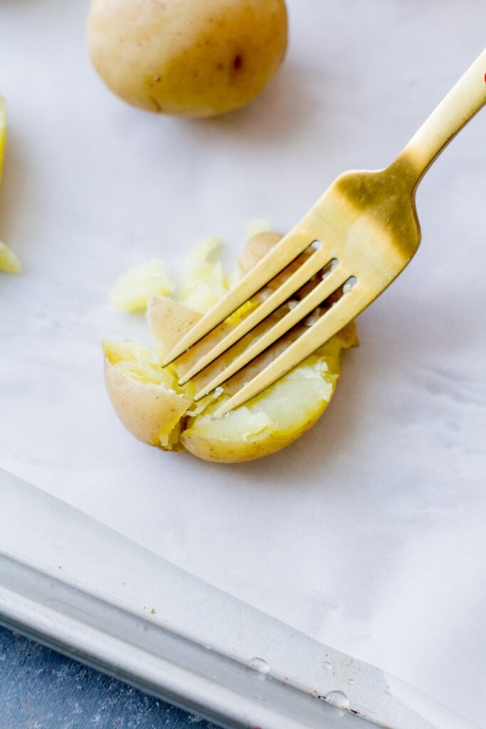 a fork pressing down a smashed potatoes