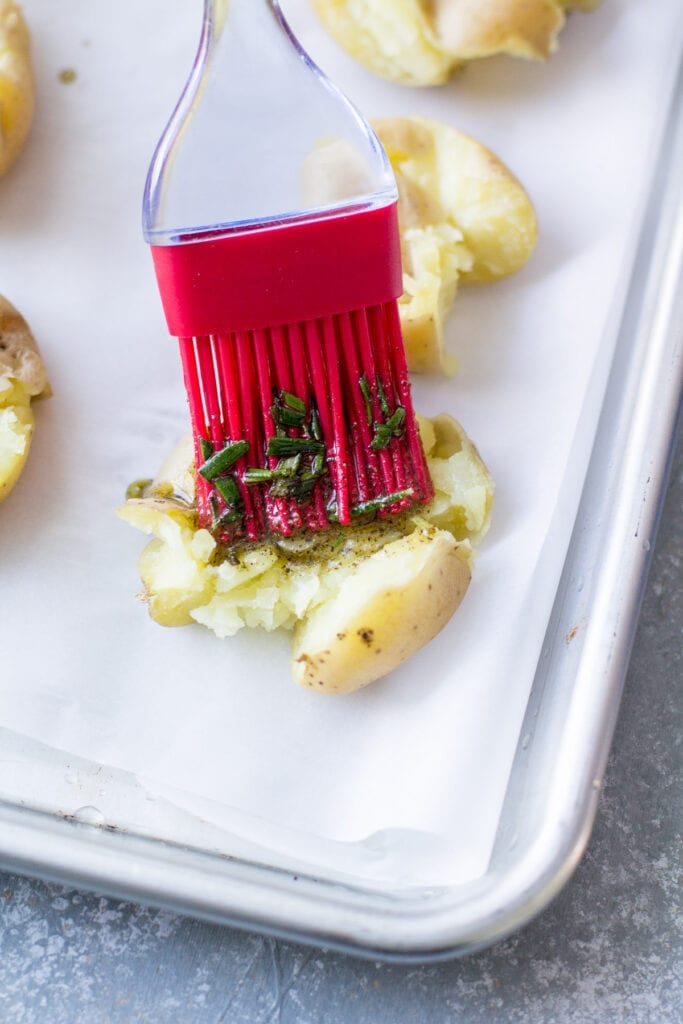 a brush coating smashed potatoes with olive oil