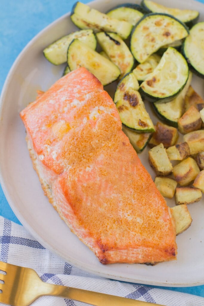 A close up of a piece of honey salmon on a white plate with zucchini and potatoes off to the side