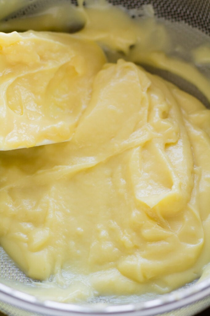 italian cream being pushed through a strainer with a spatula