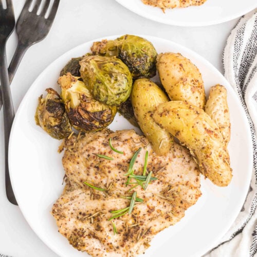 maple mustard chicken on a white plate with brussels sprouts and potatoes on a grey background