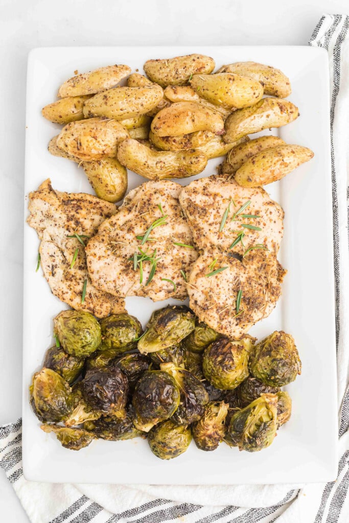 A white platter with sheet pan maple mustard chicken and roasted vegetables (brussels sprouts and potatoes) on it