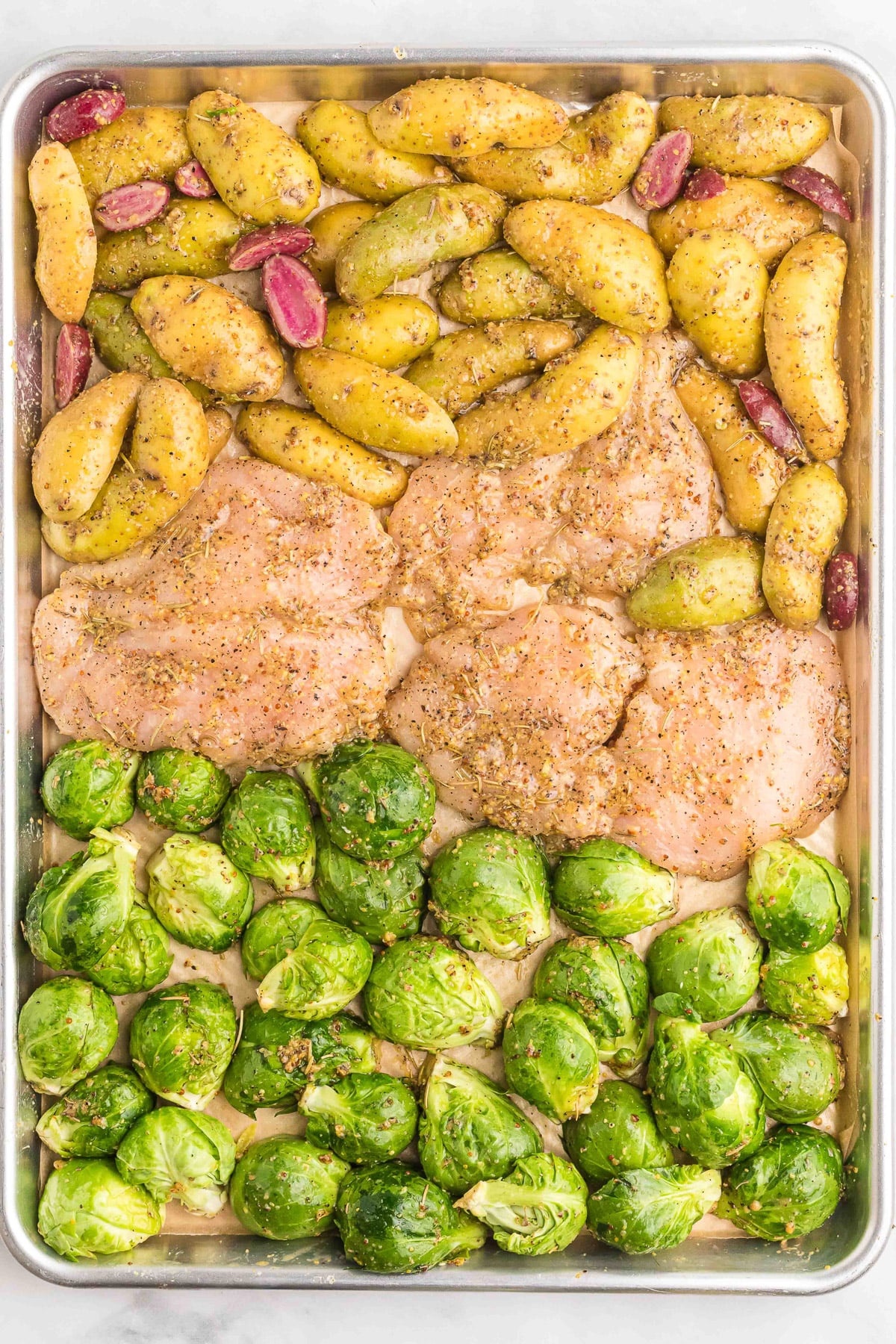 maple mustard chicken breasts, brussels sprouts and potatoes on a sheet pan before baking