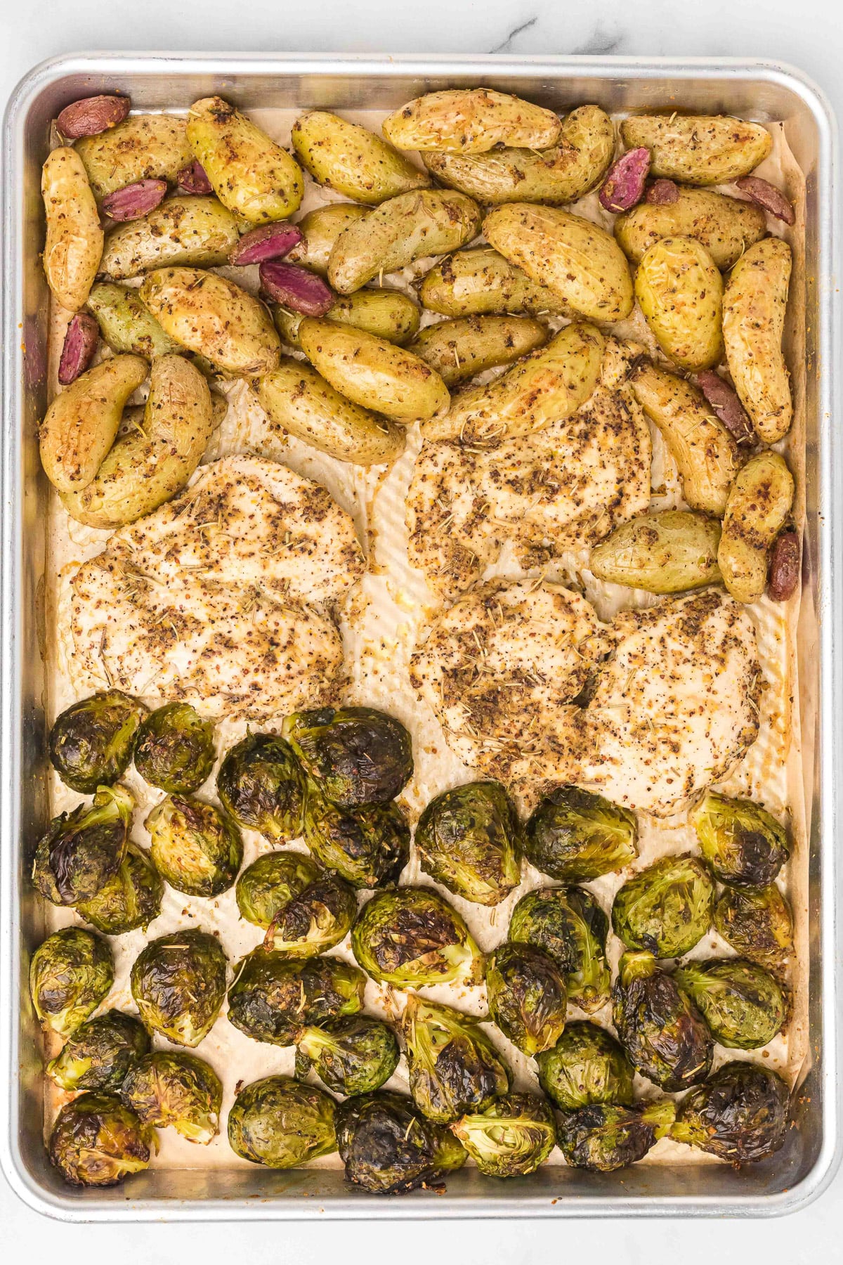 maple mustard chicken breasts, brussels sprouts and potatoes on a sheet pan after baking with a golden color