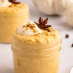 Easy Pumpkin Overnight Oats Recipe in two small clear mason jars topped with cream, pumpkin spice, and a star anise.