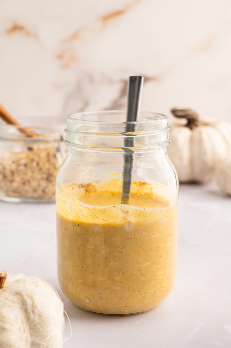A glass mason jar with pumpkin overnight oats that have been mixed together, but not fully absorbed. 