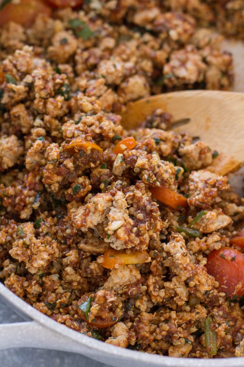 Quinoa stuffing for bell peppers being stirred with a wooden spoon in a skillet.