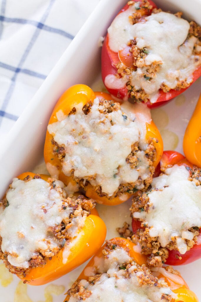 A close up of quinoa stuffed peppers in a white baking dishe with a blue checked linen off to the side.