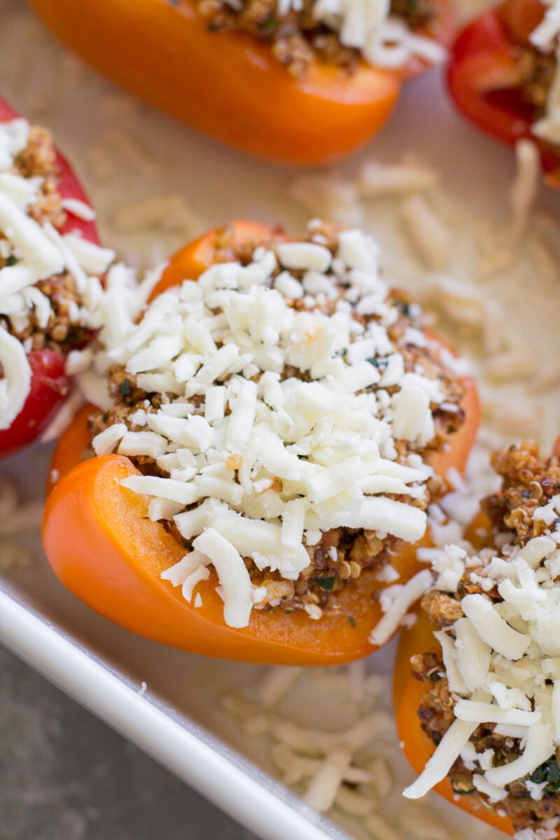 Uncooked quinoa stuffed peppers topped with cheese in a baking dish.