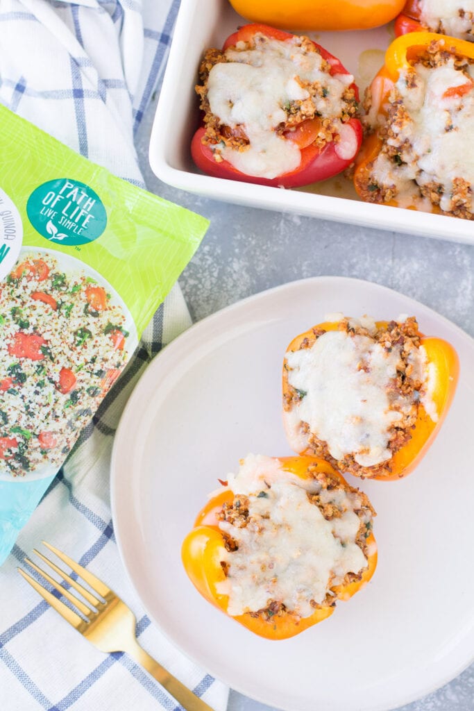 An overhead shot of stuffed peppers on a white plate with a bag of quinoa and a big baking dish of peppers off to the side.