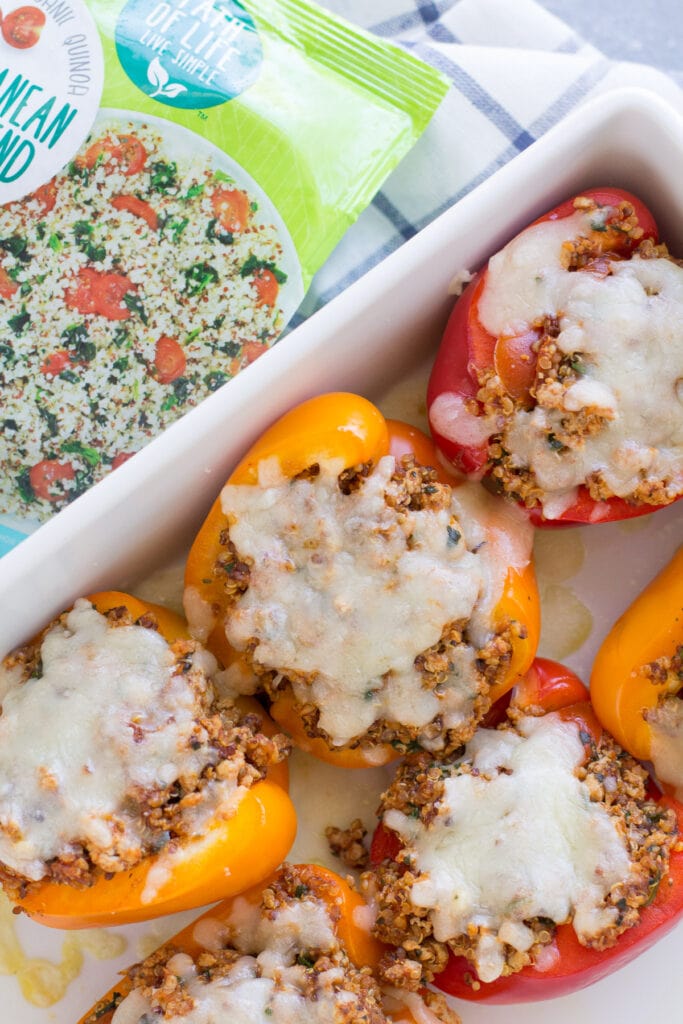 An overhead shot of a dish of stuffed peppers with a bag of quinoa off to the side.