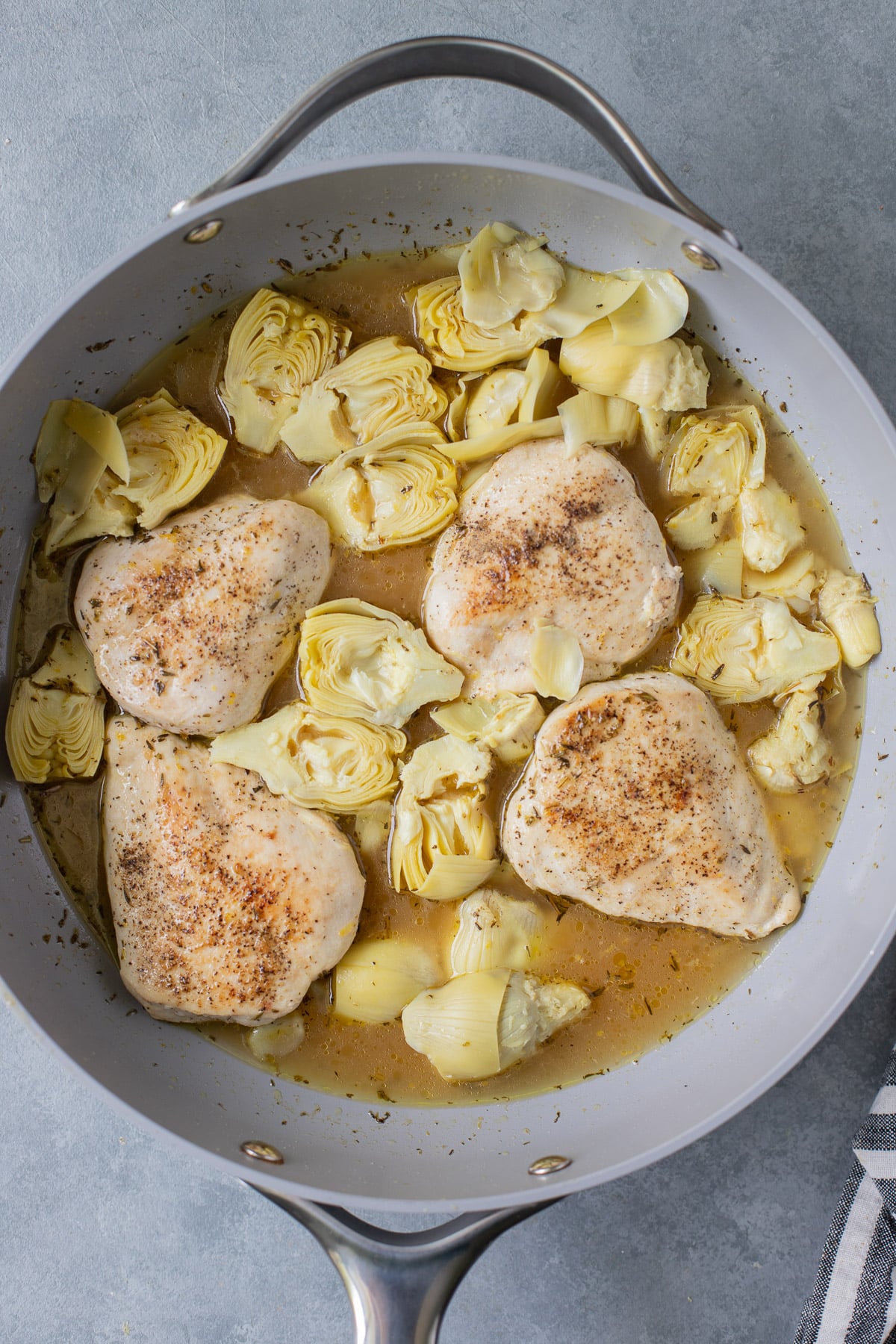 An overhead shot of lemon artichoke chicken in a pan on a grey background