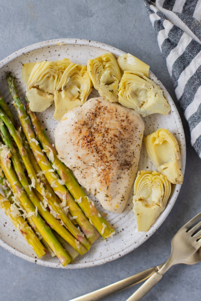 An overhead shot of Lemon Artichoke Chicken with artichokes on a plate with asparagus