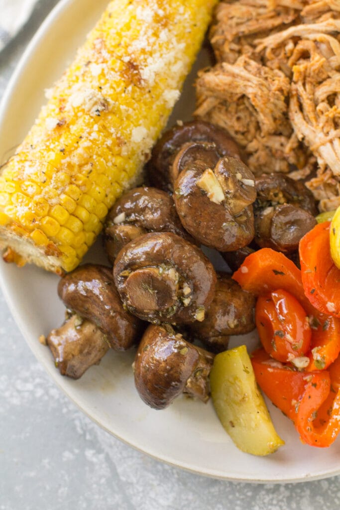 A close up of grilled mushrooms on a plate with corn and roasted veggies