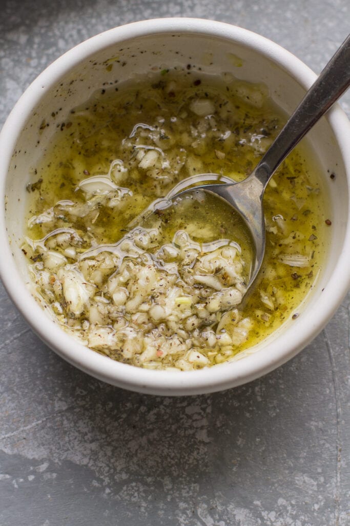 a small white bowl of olive oil and garlic being mixed together for garlic parmesan corn