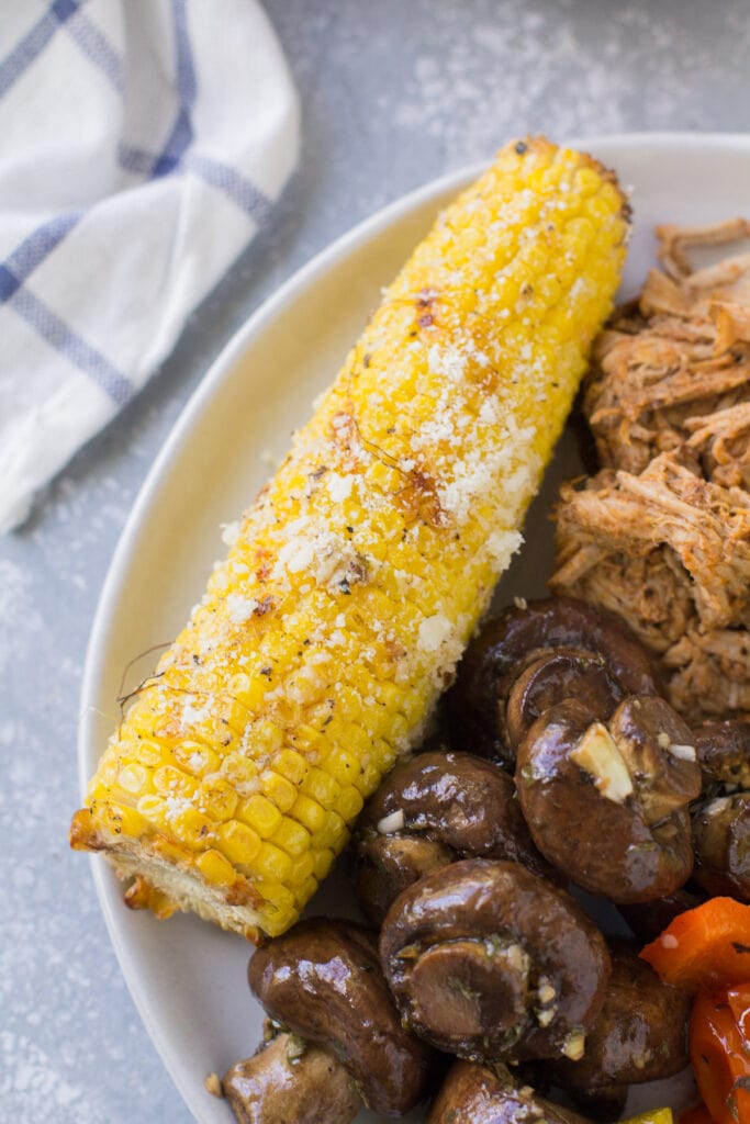 Grilled corn on the cob on a white plate with veggies off to the side
