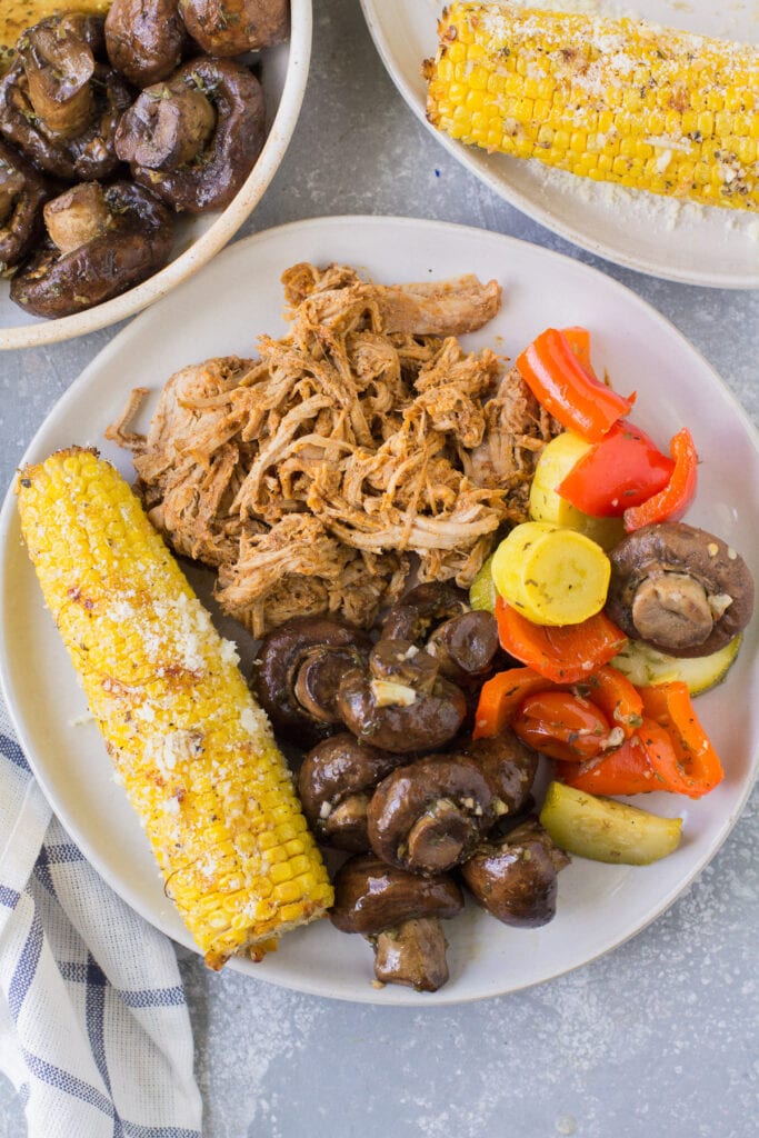 Parmesan Corn on the cob on a white plate with grilled veggies and pulled pork