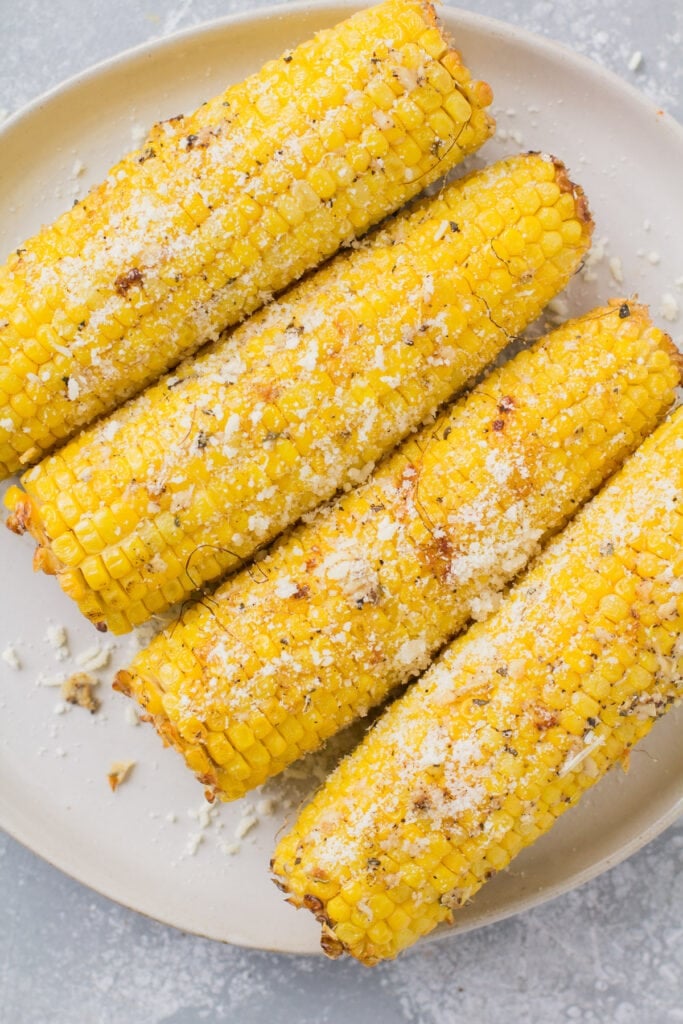 Garlic parmesan grilled corn on a white plate on a grey background