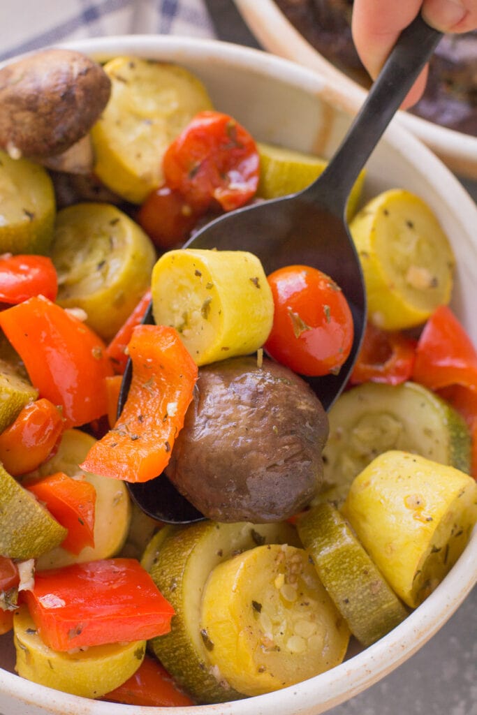 A black spoon scooping up grilled vegetables