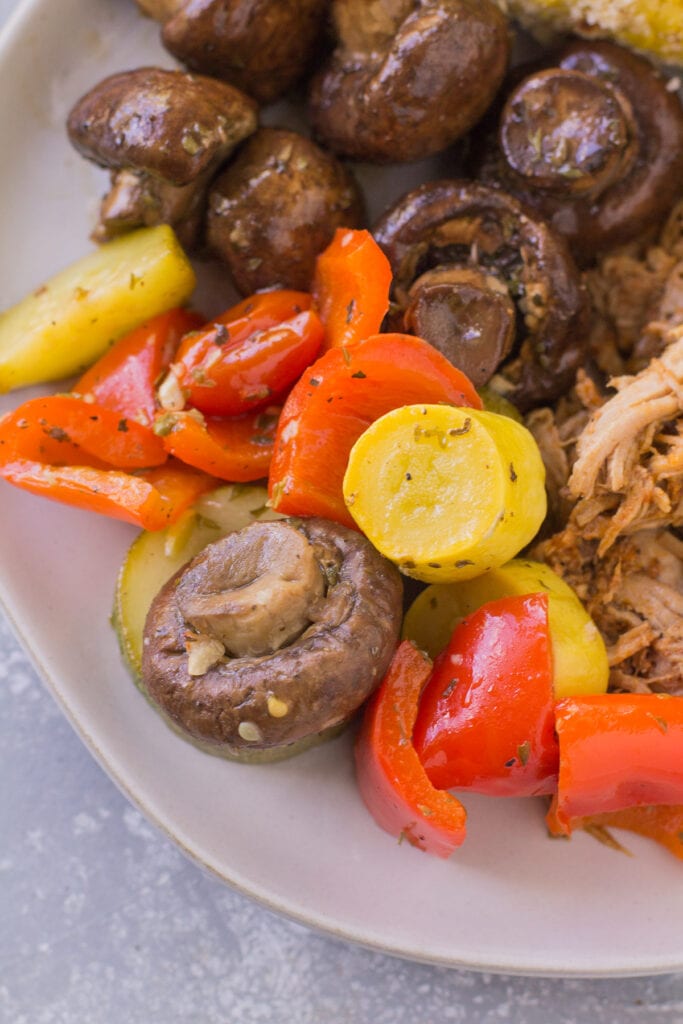 A close up of grilled vegetables in foil on a white plate