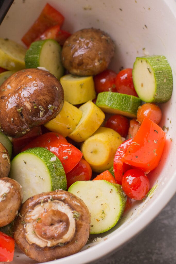 Vegetables in a white bowl being mixed together for grilled veggies