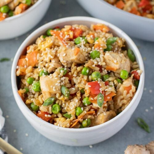 An overhead bowl of Healthy Fried Rice on a grey background with fried rice in the background