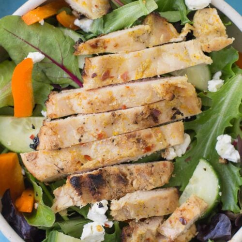 Spicy Honey Citrus Chicken in a white bowl on top of a salad with a blue background