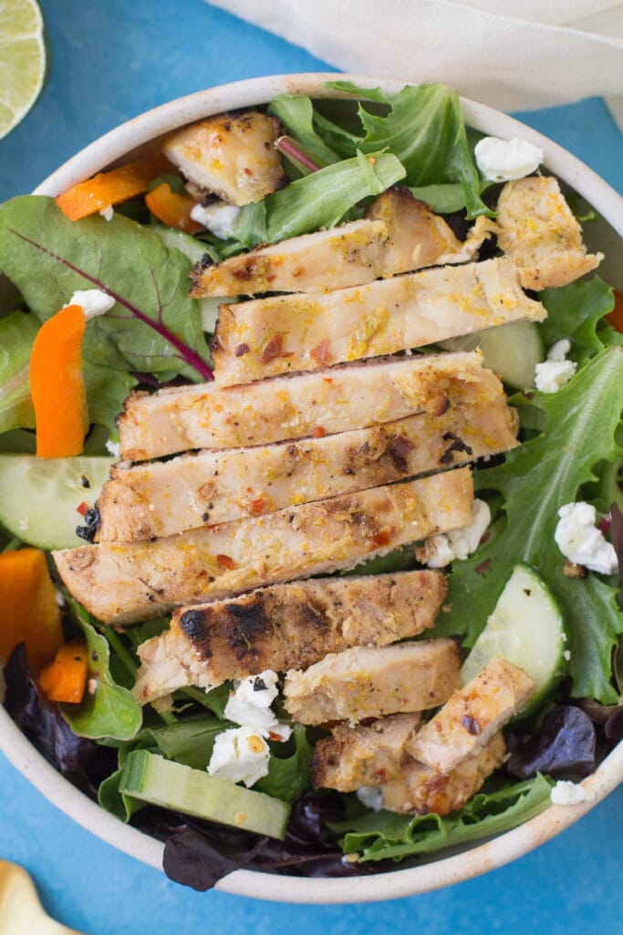 Spicy Honey Citrus Chicken in a white bowl on top of a salad with a blue background