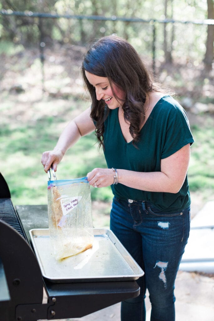 A girl grilling - putting chicken on the grill.