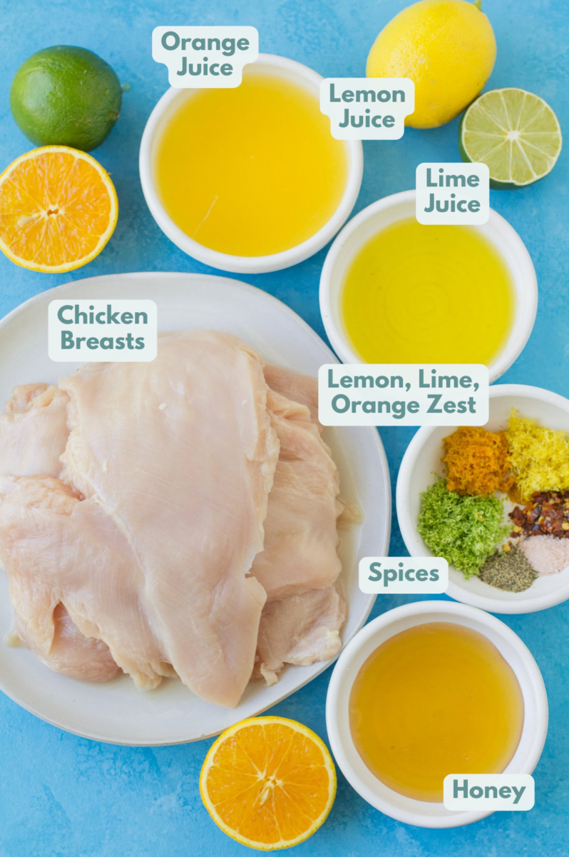An overhead shot of ingredients for Honey Citrus Chicken in small white bowls on a blue background.