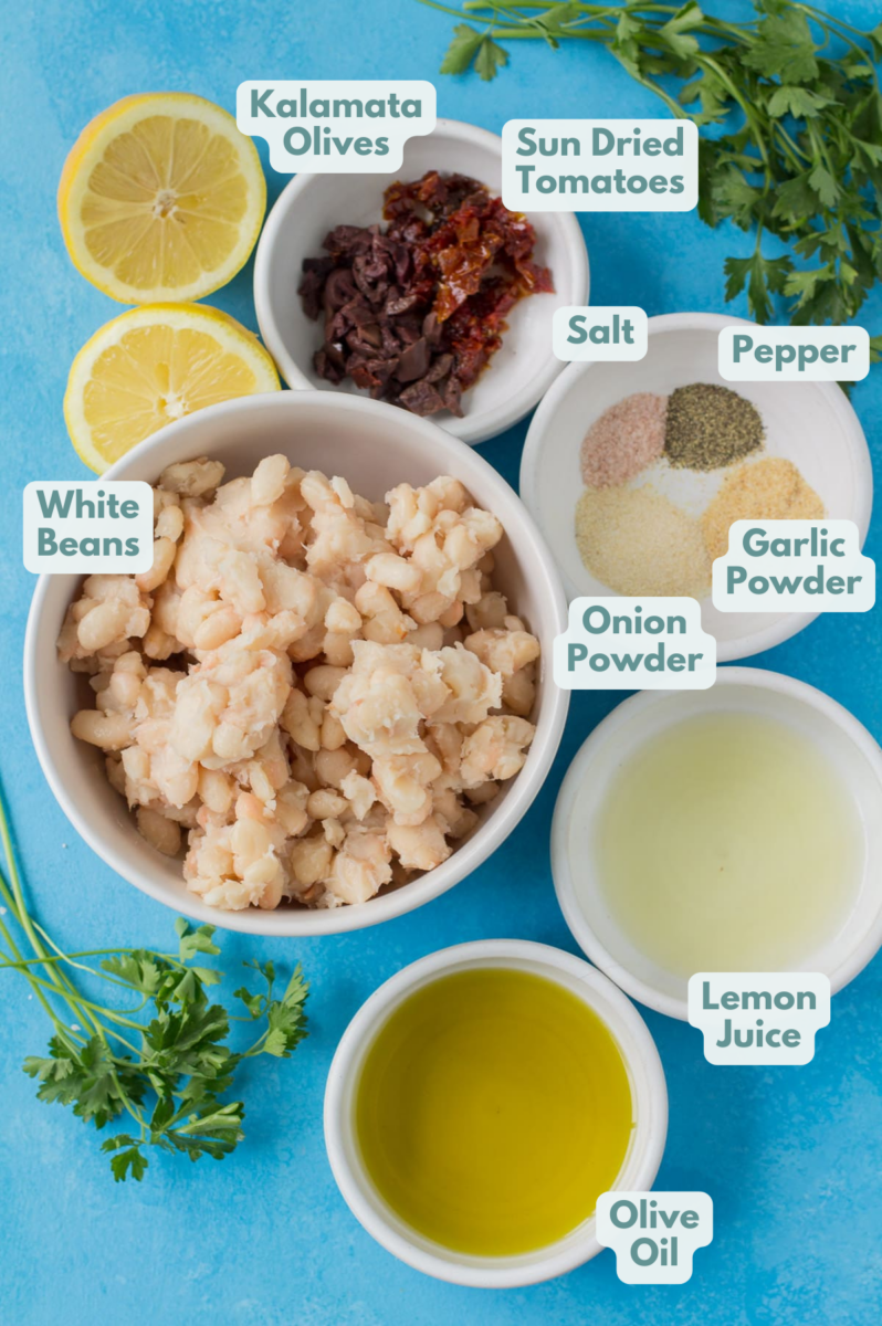 Ingredients for white bean hummus in small white bowls on a bright blue background