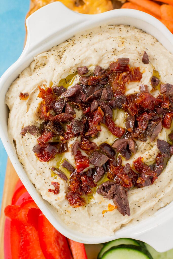 An overhead close up image of white bean dip on a cutting board with veggies