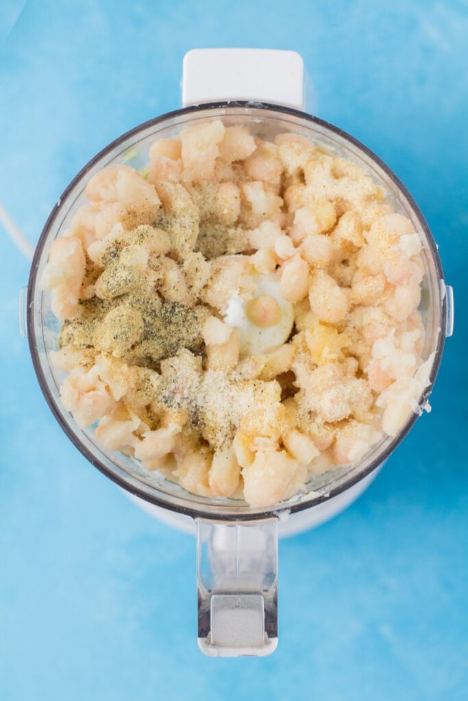 An overhead image of white bean hummus in a food processor on a blue background