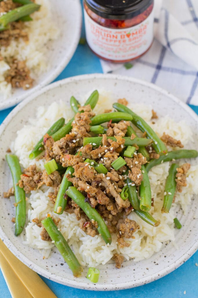 An overhead image of two plates of ground turkey stir fry with bomba sauce in the background