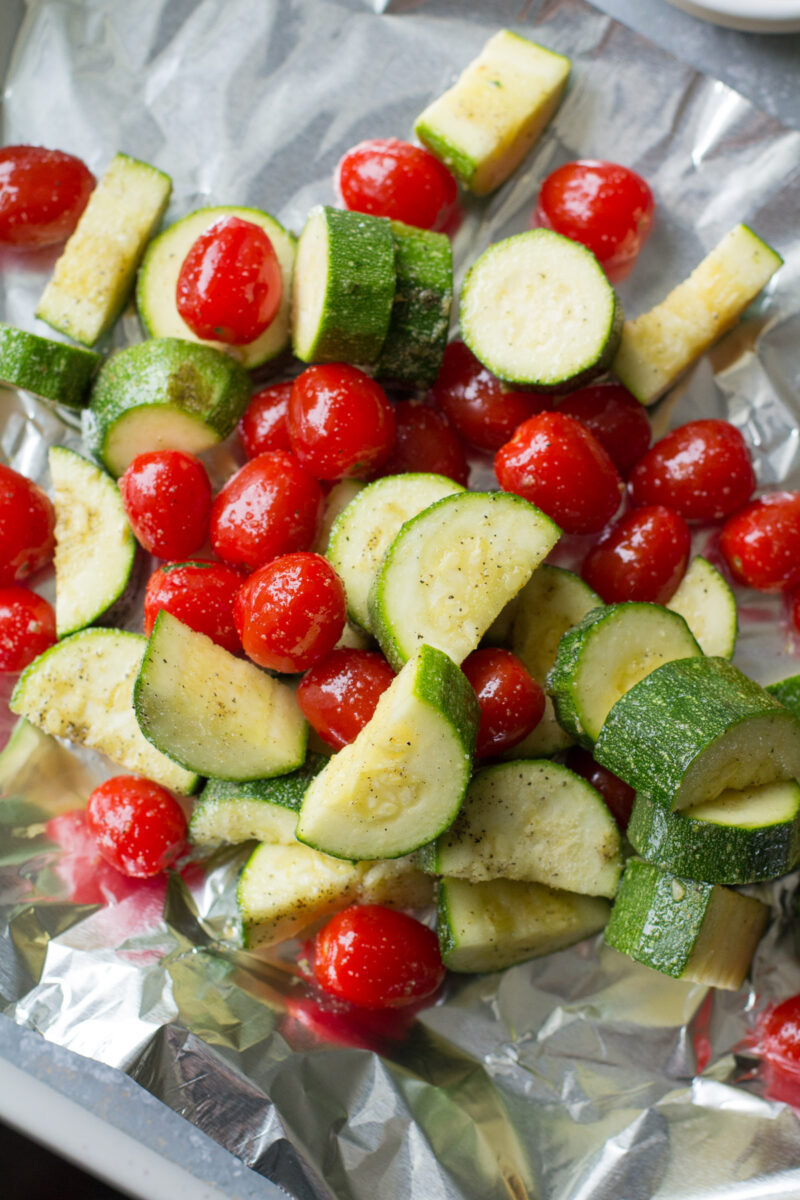 Zucchini and cherry tomatoes tossed in oil and spices on a piece of foil.