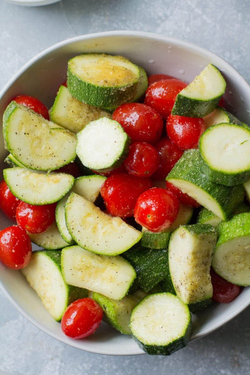 Zucchini and Cherry Tomatoes tossed in oil and spices in a large bowl.
