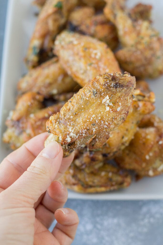 A hand holding up Parmesan Chicken Wing off a plate of wings