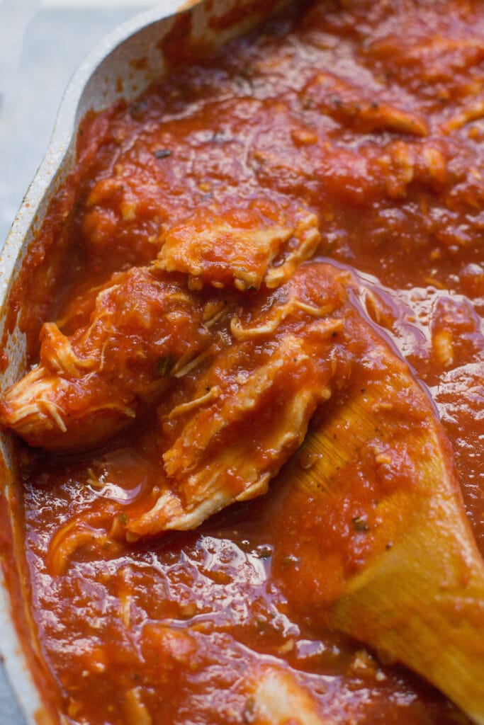 Chicken Tomato Sauce in a grey pan with a wooden spoon scooping up a serving