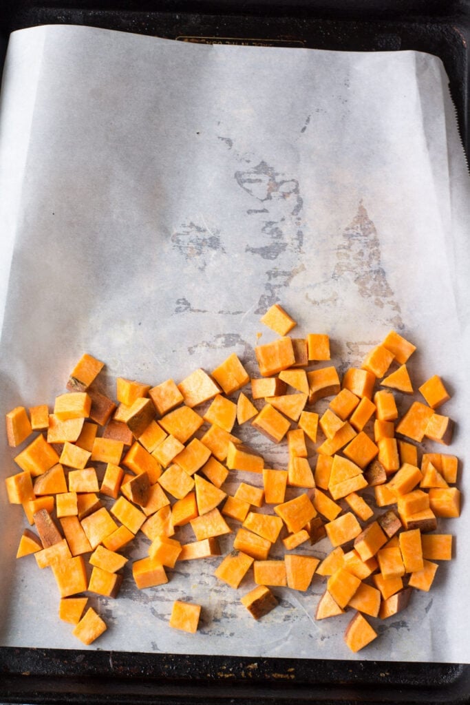 a parchment paper prepared sheet pan with sweet potatoes before being cooked for a sheet pan breakfast