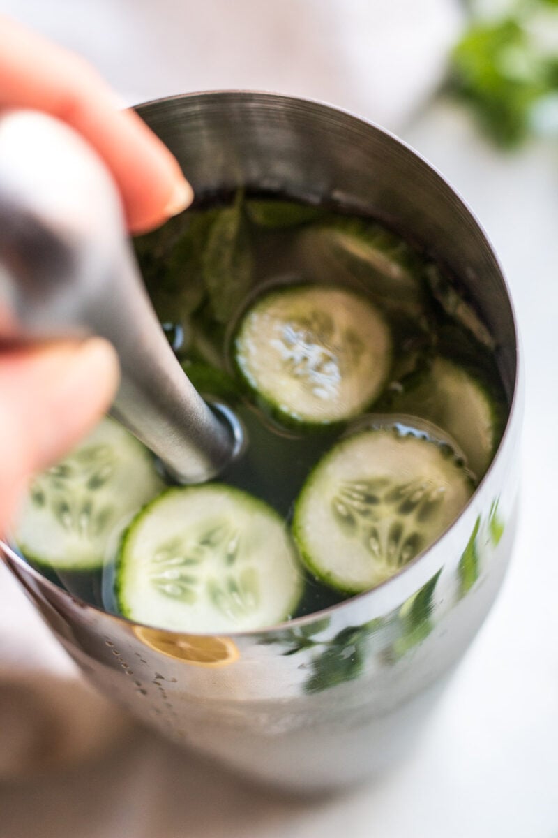 A hand stirring a lemonade cucumber cocktail in a shaker.