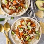 Ground Beef and Sweet Potato Chili in small white bowls with jalapenos, gold spoons, avocados and chips off to the sides