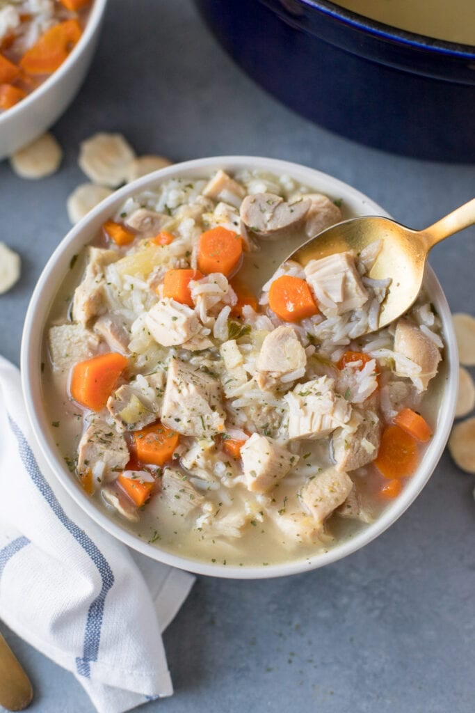 Leftover Turkey Soup in a white bowl with a gold spoon taking a spoonful out of it.