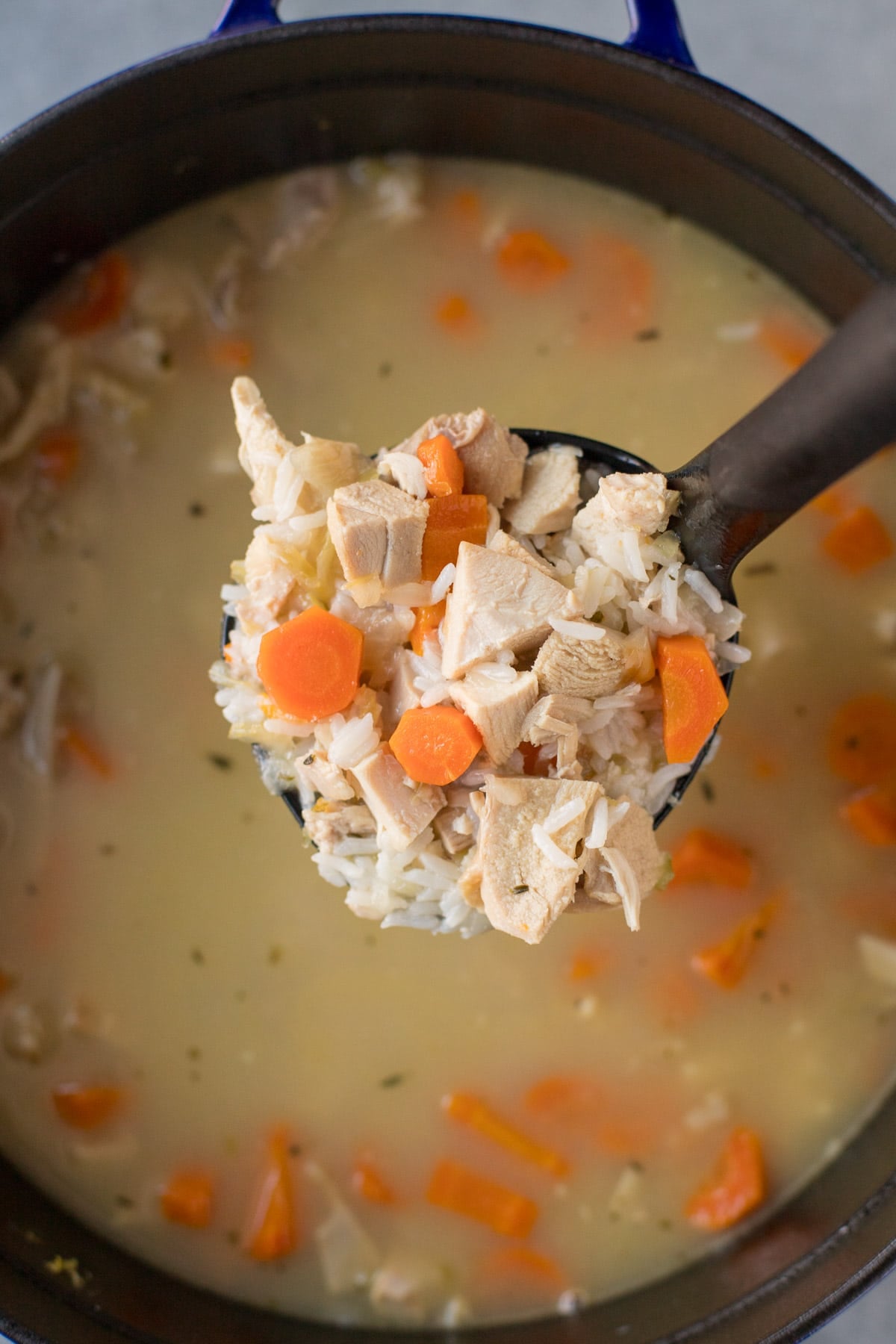 A black ladle holding up a scoop of leftover turkey soup from the pot